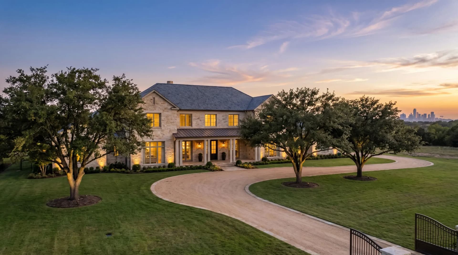 Ultra-luxury North Texas estate at twilight behind a gated drive, framed by mature live oaks — the architectural language of Highland Park and Preston Hollow.