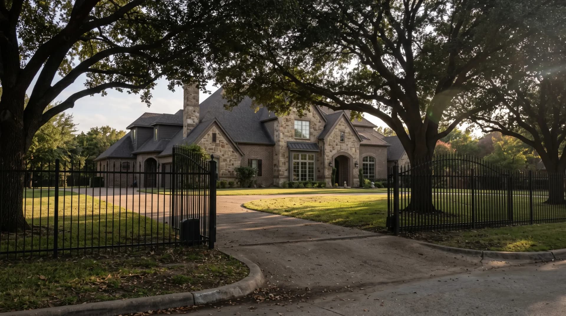 Large stone luxury estate behind an iron gate under mature live oaks, illustrating property taxes on high-value homes in Texas.